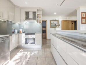 A modern kitchen with white cabinetry, a stainless steel range hood, and a built-in oven. - Villa with sea view and private pool (Salou)