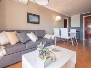 Ein Wohnbereich mit grauem Sofa, weißen Sesseln, einem weißen Couchtisch mit Pflanze und einem Gemälde an der Wand.