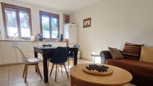Zona pranzo con tavolo, sedie, un tavolino rotondo in legno con una ciotola di olive, un divano e una cucina sullo sfondo.