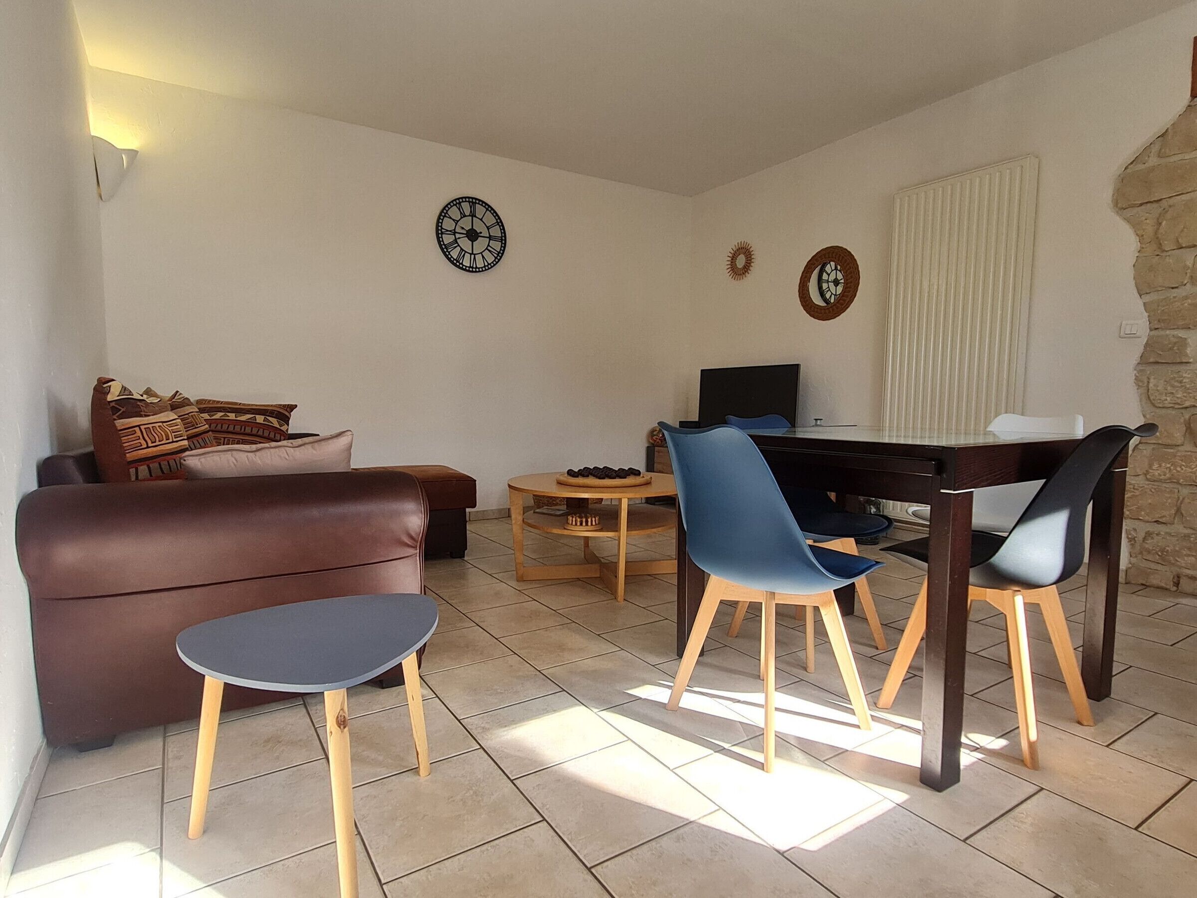 A living room with a brown sofa, a small round table, a TV, and two chairs.