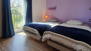 Camera da letto con due letti, una finestra con tende, una lampada e vista sul verde.