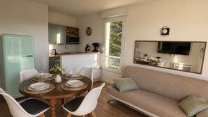 Un espace de vie compact comprenant un coin repas, une kitchenette, un canapé et un téléviseur fixé au mur.