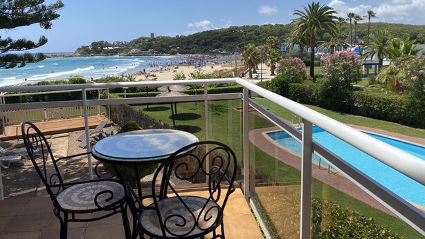 A balcony with a view of a beach, a pool, and a dining area with chairs and a table. - Seafront apartment with views - NOR guests (La Mora)