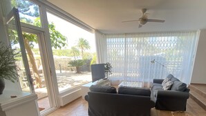 A living room with a sofa set, a TV, a ceiling fan, and a view of the outdoors through large windows. - Seafront apartment with views - NOR guests (La Mora)