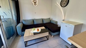 Una sala de estar moderna con un sofá seccional, una mesa de centro, un refrigerador pequeño y un reloj fijado a la pared.