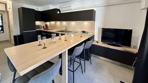 Una cocina moderna con una isla central, un comedor con sillas, un televisor y una pequeña isla de cocina con electrodomésticos.