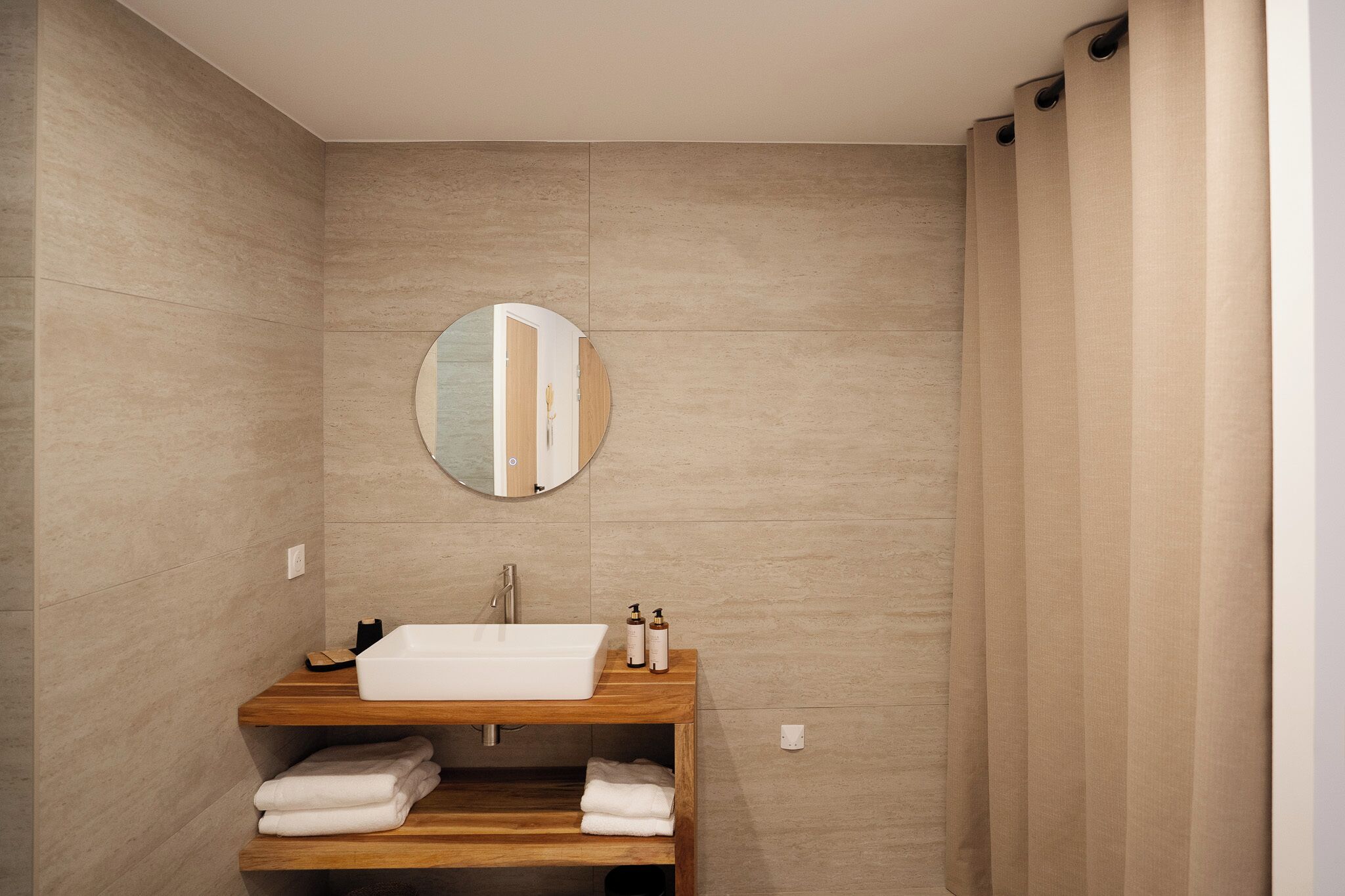 A bathroom with a wooden vanity, a round mirror, and a shower curtain.