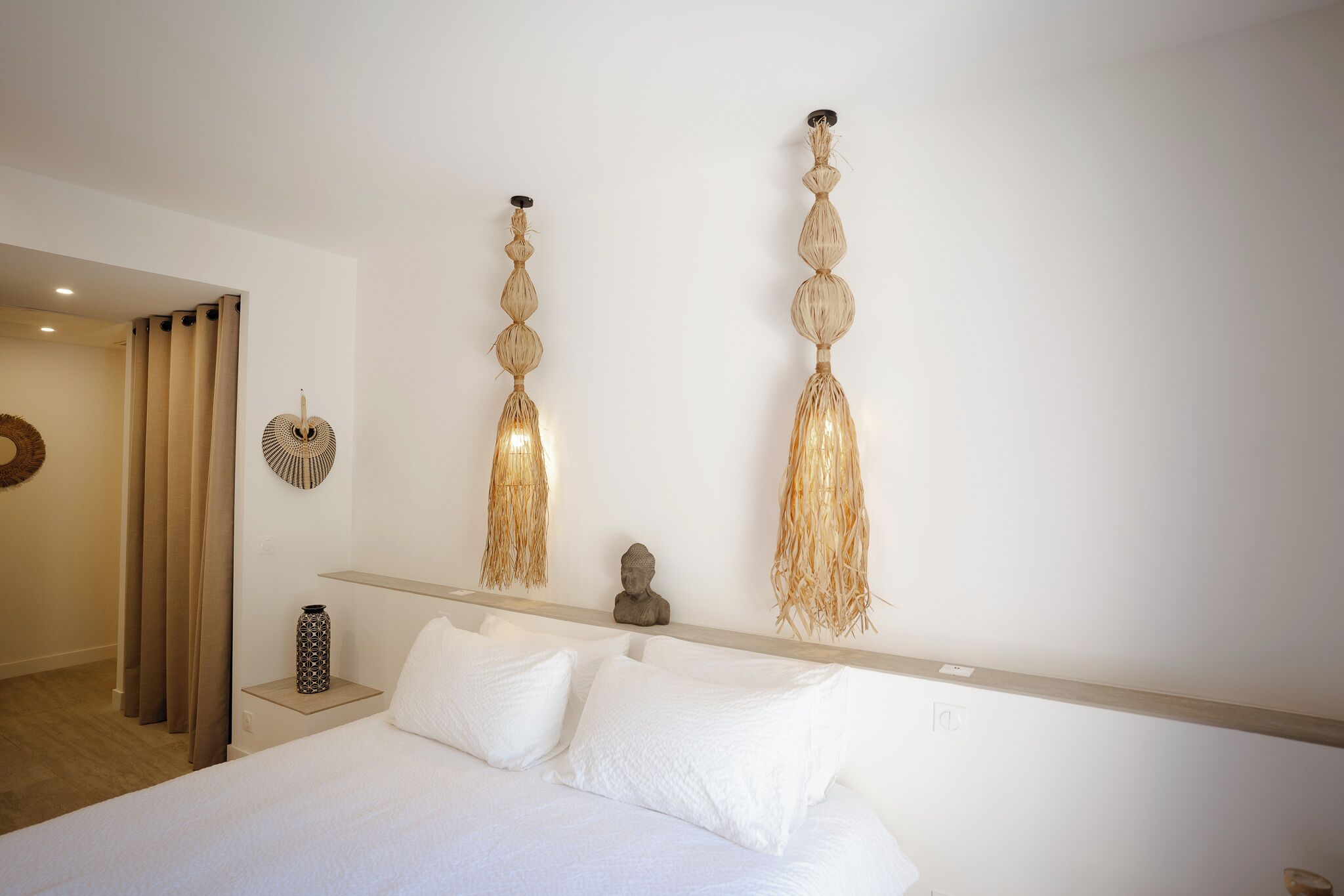 Een hotelkamer met een bed, een nachtkastje, een aan de muur bevestigd beeldhouwwerk en twee wandlampen.