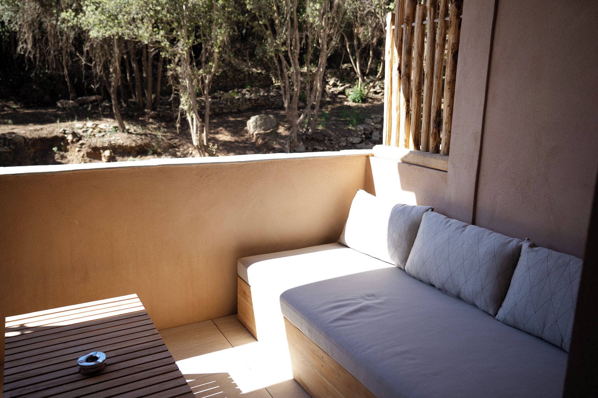 Un balcon doté d’un espace salon avec des coussins, d’une petite table et offrant une vue sur un paysage naturel.