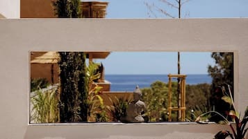 Ein moderner Sitzbereich im Freien mit Blick auf das Meer und einem Gebäude im Hintergrund.
