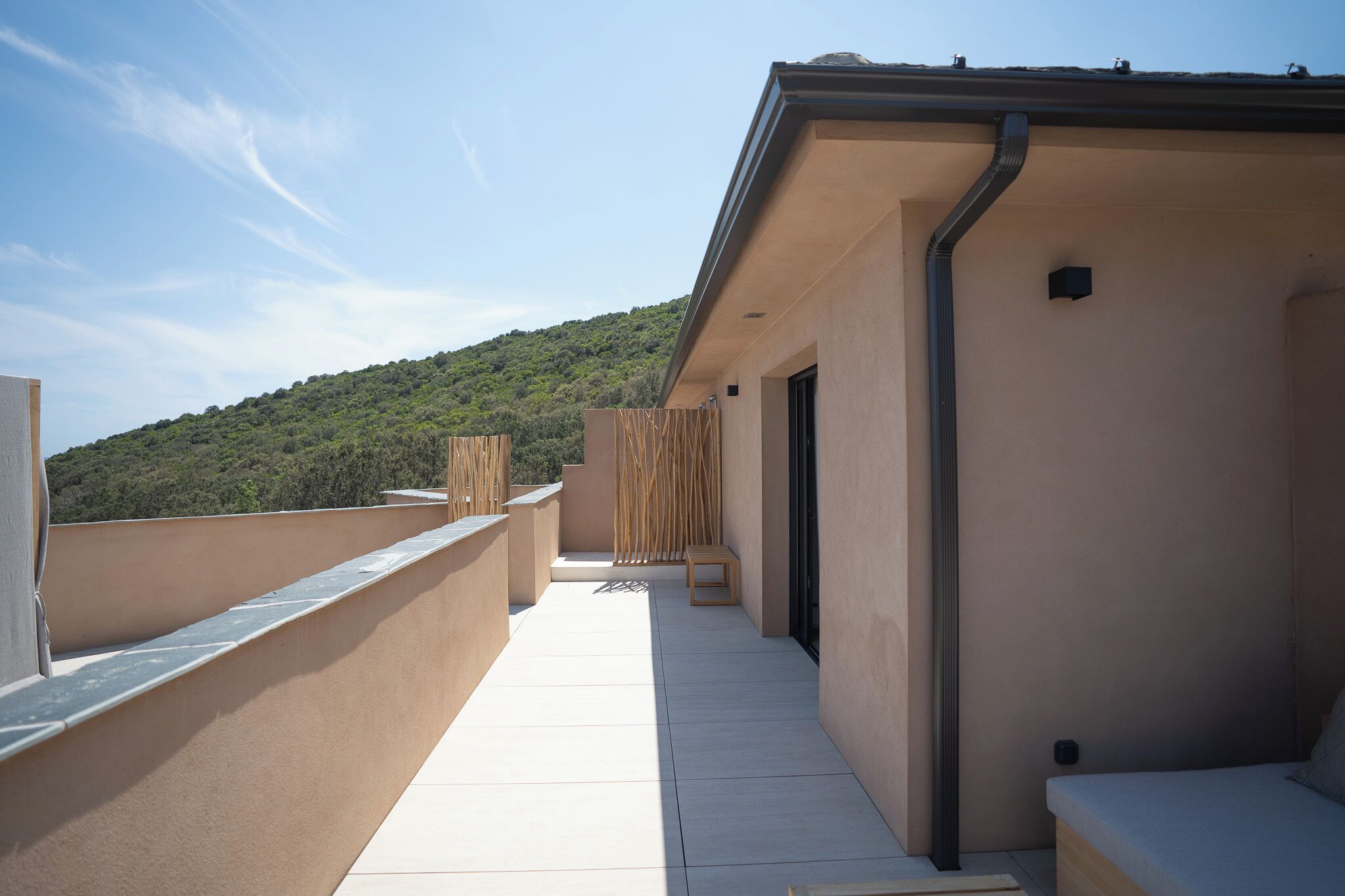Una terraza en la azotea con vistas a una colina verde, una valla de madera y un pequeño espacio para sentarse.