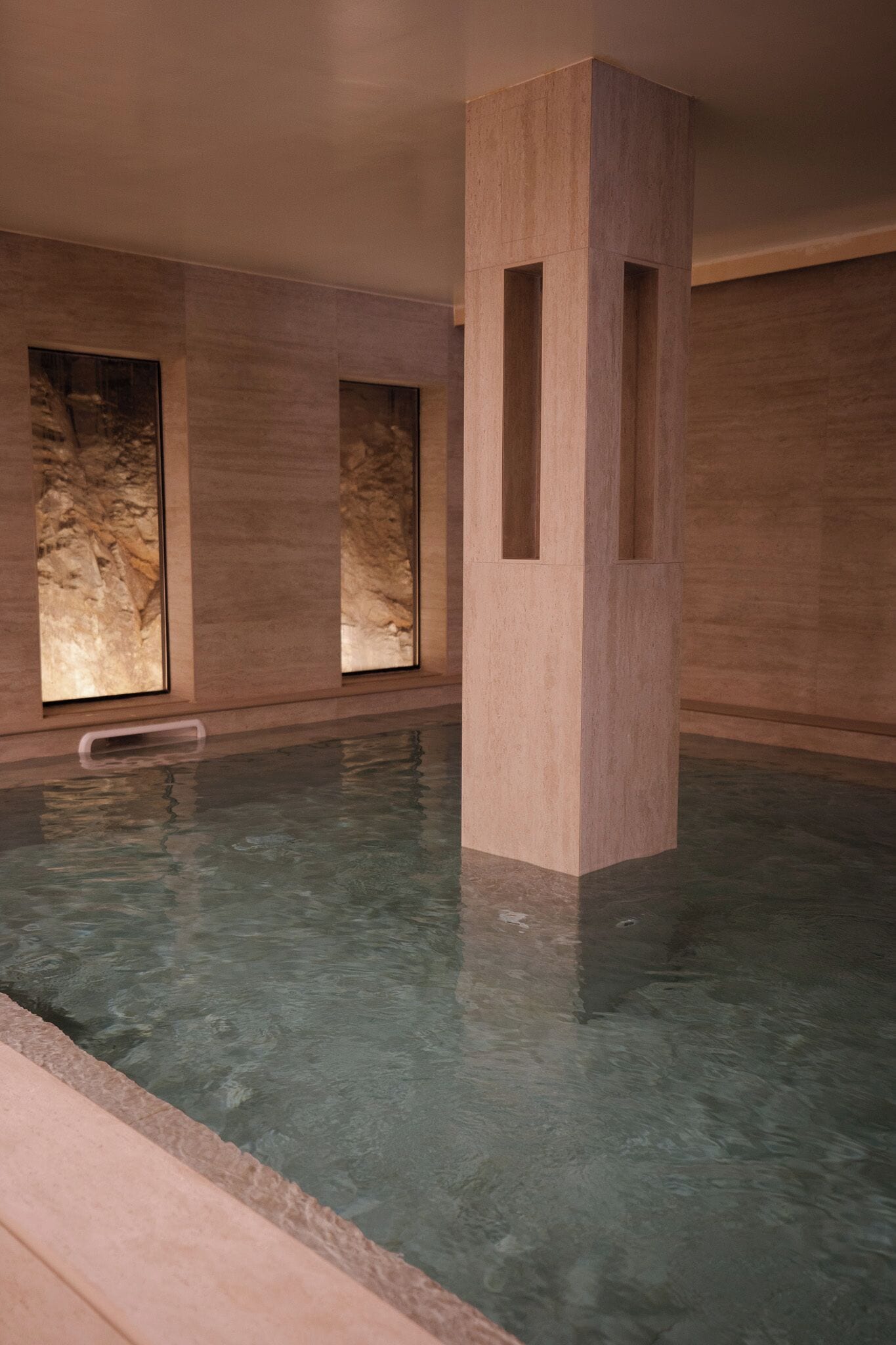 A swimming pool with clear water, surrounded by stone walls and large windows.