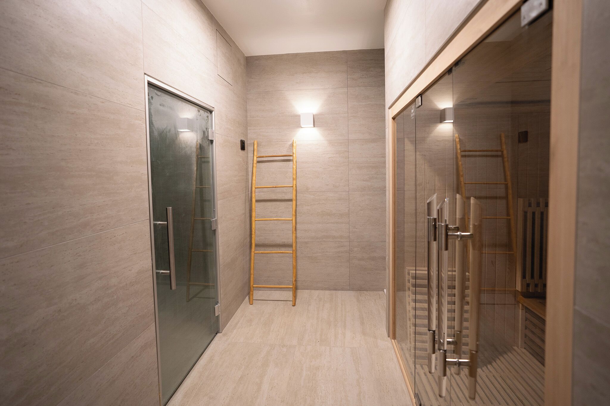A modern bathroom with a glass shower enclosure, a wooden ladder, and a light fixture on the wall.
