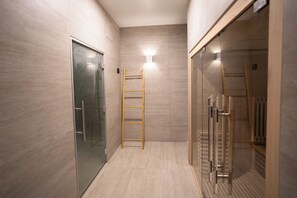 A modern bathroom with a glass shower enclosure, a wooden ladder, and a light fixture on the wall.