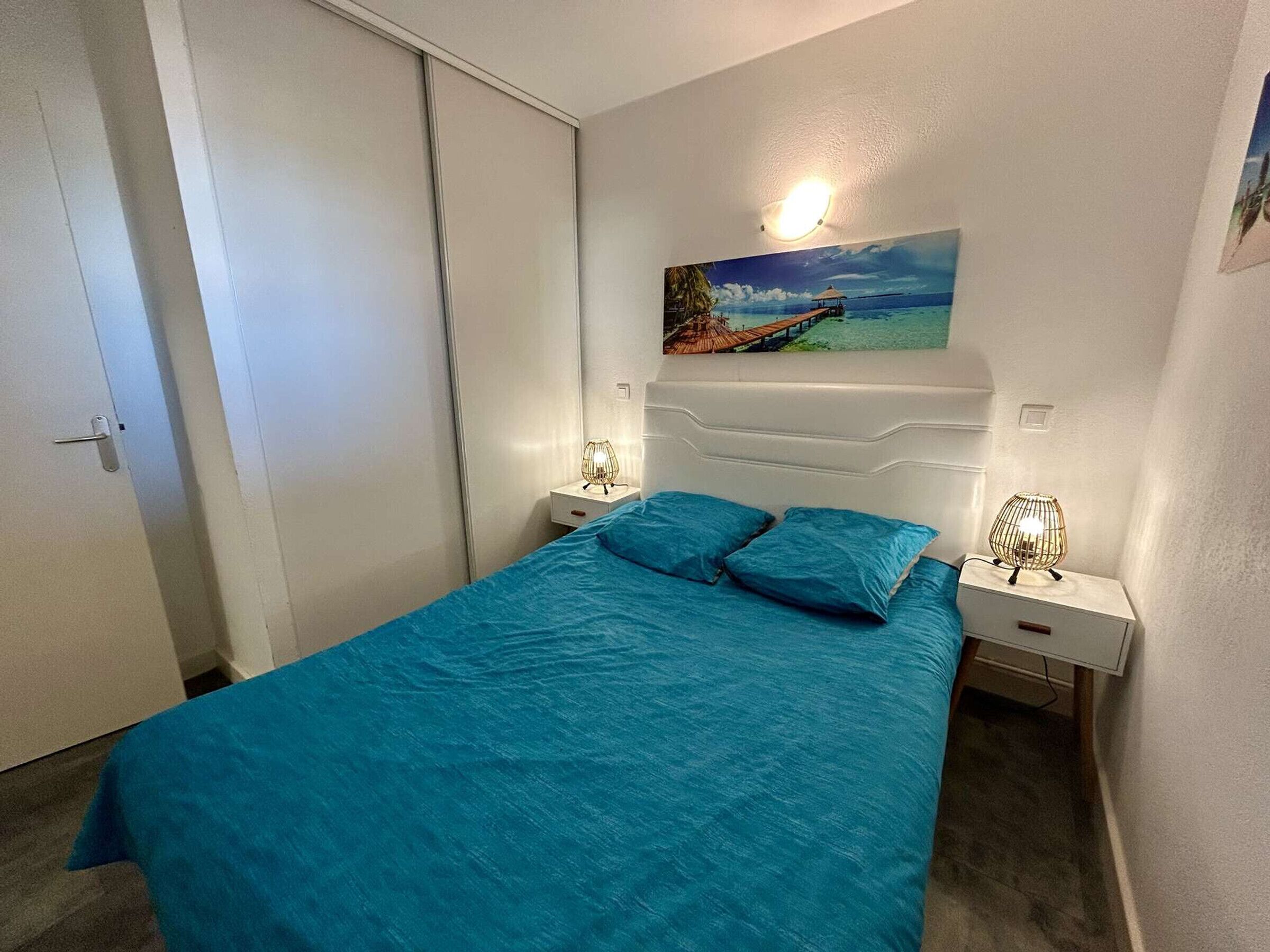 Une chambre à coucher avec un lit, deux tables de chevet, une commode, un tableau au mur et une porte.
