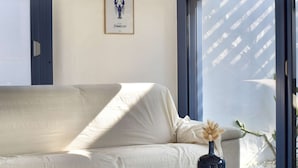 A room with a white sofa, a small table with a vase and a book, and a window with a view of a building. - House near the sea - 5 guests (Noirmoutier-en-l'Île)