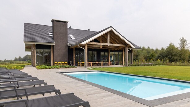 Ett modernt hus med en swimmingpool, solstolar och en täckt uteplats.