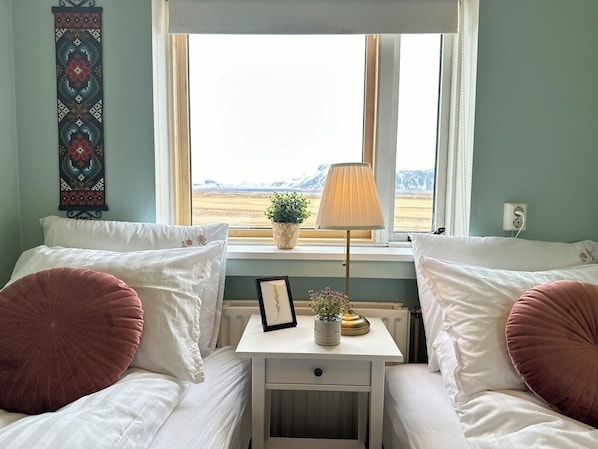 A bedroom with two beds, a bedside table with a lamp, a framed picture, and a plant. - Selid Farm Stay (Borgarbyggð)
