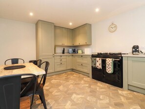 A kitchen with a dining table, chairs, cabinets, a clock, and appliances. - Cowside Farm (Settle)