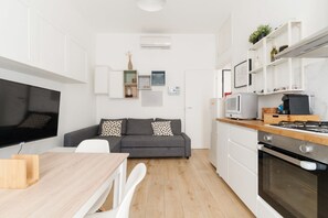 Een moderne keuken met een eethoek, een grijze bank en een flatscreen televisie.