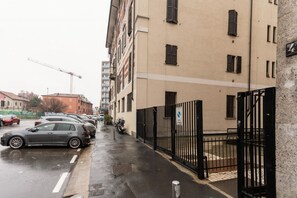 Een smalle straat met geparkeerde auto's en een hek bij een gebouw.