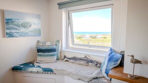 Een slaapkamer met uitzicht op zee, een bed met een gestreept kussen, en een klein plankje met een vogelfiguurtje.