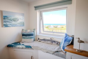 Ein Schlafzimmer mit Meerblick, ein Bett mit einem gestreiften Kopfkissen und eine kleine Ablagefläche mit einer Vogelstatue.