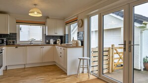 Een moderne keuken met witte kastjes, een houten aanrechtblad, een hanglamp en een schuifdeur naar een terras.
