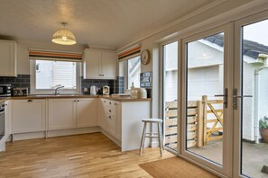 Eine moderne Küche mit weißen Schränken, einer Holz Arbeitsplatte, einer Hängeleuchte und einer Schiebetür zu einer Terrasse.