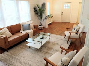 A living room with a sofa, armchairs, a glass coffee table, a potted plant, and a door. - Rose of Wilmington - We Love Dogs - Sleeps 9 (Wilmington)