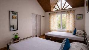 Ein Schlafzimmer mit zwei Betten, einem Fenster mit floralem Vorhang, einem Spiegel und einer Zimmerpflanze.