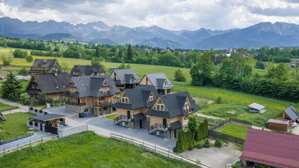 A cluster of traditional wooden houses with steep roofs, surrounded by lush greenery and mountains in the background. - EcoWood Tatry by Jasek Premium (Poronin)
