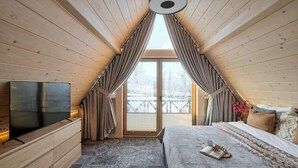 A cozy attic bedroom with a large window, a flat-screen TV, and a bed with a blanket and pillows. - EcoWood Tatry by Jasek Premium (Poronin)