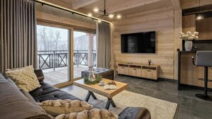 A modern log cabin interior with a living area, a flat-screen TV, a dining area, and a balcony with a view. - EcoWood Tatry by Jasek Premium (Poronin)