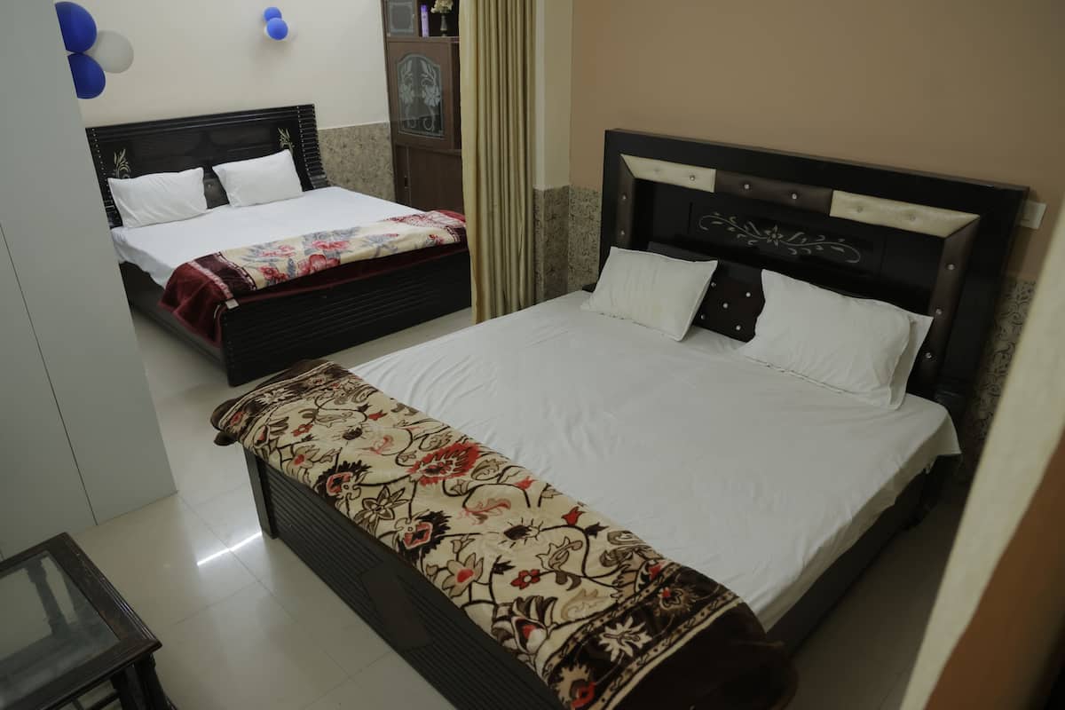 Two beds with white linens, a floral-patterned bedspread on one, and a wooden headboard with a decorative design.