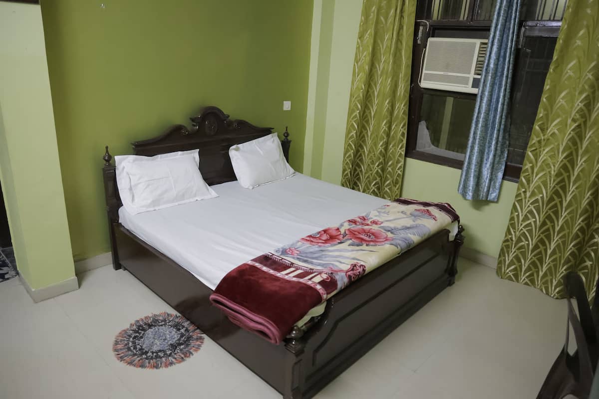 A neatly made bed with white linens and a floral blanket, a round patterned rug, and green patterned curtains.