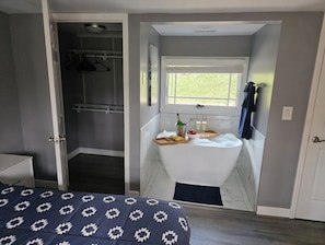 A bedroom with a bed, a walk-in closet, and a bathroom with a bathtub. - Grand opening to gorgeous Asheville house! (Asheville)