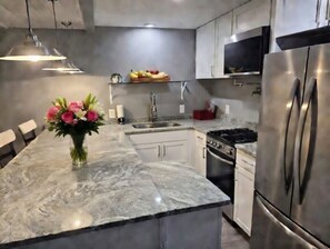 A kitchen with a marble countertop, stainless steel appliances, and a vase of flowers. - Grand opening to gorgeous Asheville house! (Asheville)