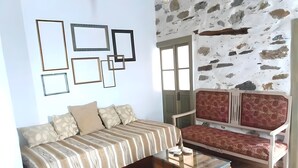 A room with a bed, a sofa, a wooden chest, and a stone wall. - Apartment 'The Balcony Of Bougainvillea' with Sea View, Wi-Fi and Air Conditioning (Ano Syros)