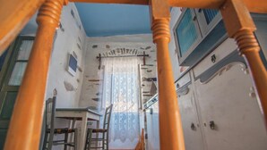 A room with a staircase, a wooden chair, a table, and a window with a curtain. - Apartment 'The Balcony Of Bougainvillea' with Sea View, Wi-Fi and Air Conditioning (Ano Syros)