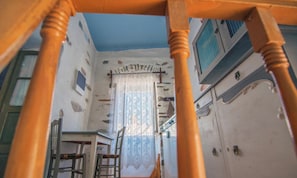 A room with a staircase, a wooden chair, a table, and a window with a curtain. - Apartment 'The Balcony Of Bougainvillea' with Sea View, Wi-Fi and Air Conditioning (Ano Syros)
