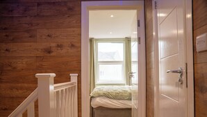 Ein Holzboden-Flur, der zu einem Schlafzimmer führt, mit Fenster, Tür und einem weißen Geländer.