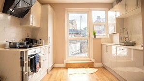 Eine moderne Küche mit Herd, Backofen und Schränken, ein Fenster mit Blick auf Gebäude und ein Holzboden.
