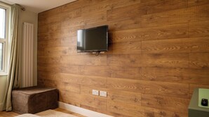 Ein modernes Zimmer mit Holzwand, einem angebrachten Fernseher, einer Steckdose und einem Fenster mit Vorhängen.