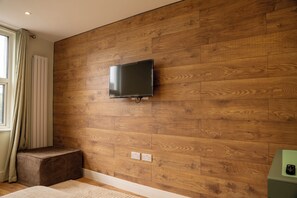 A modern room with a wooden wall, a mounted TV, a power outlet, and a window with curtains. - Chic 2BR Herne Hill Apartment - 1 Minute from Train Station to Central London! (London)