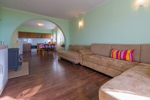 Ein Wohnzimmer mit einer Couch, einem Esstisch mit Stühlen und einer Küche im Hintergrund.