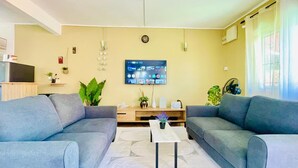 Olohuoneessa on kaksi sohvaa, sohvapöytä, televisio ja seinällä oleva kello.