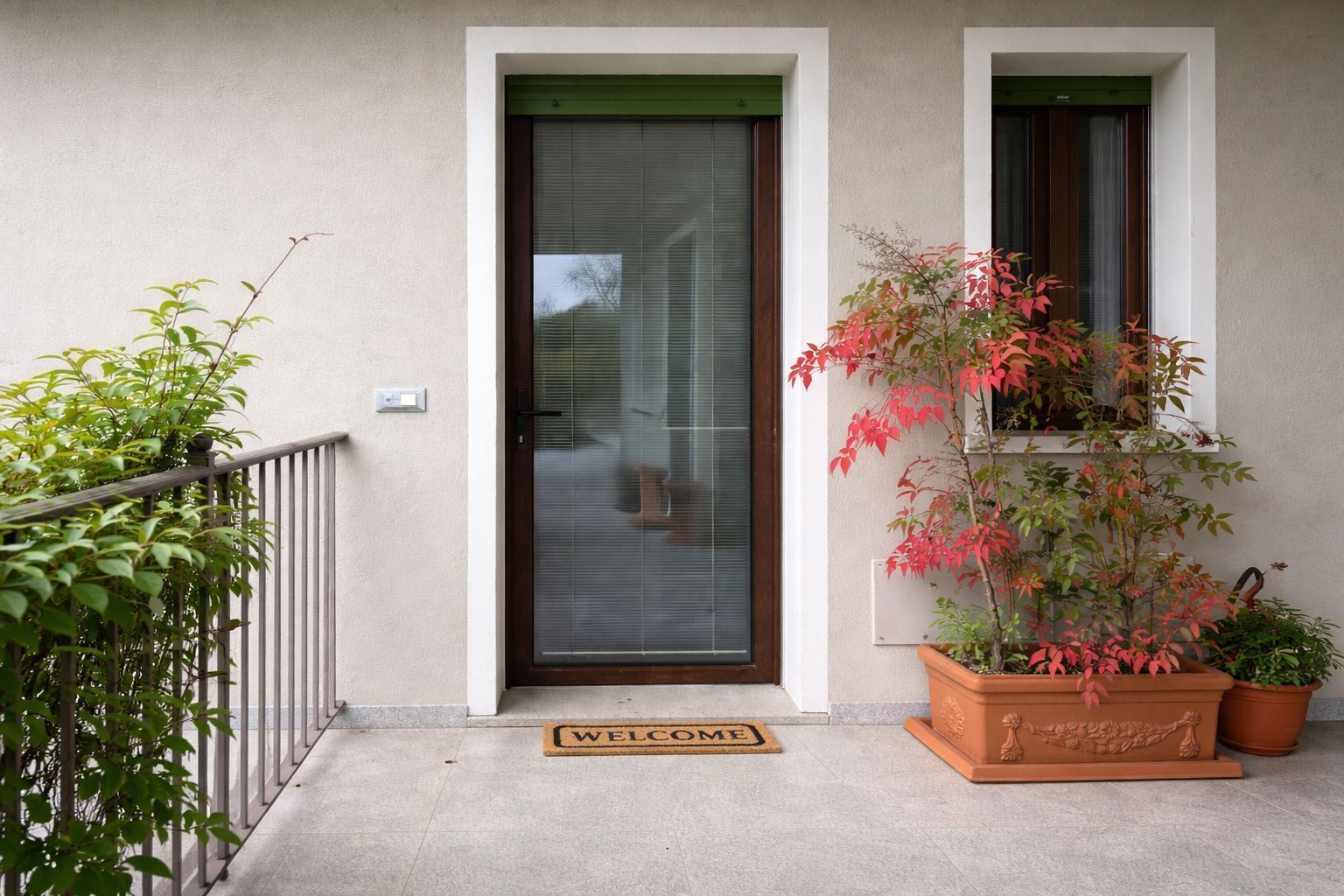 A residential entrance with a door, a welcome mat, and potted plants.