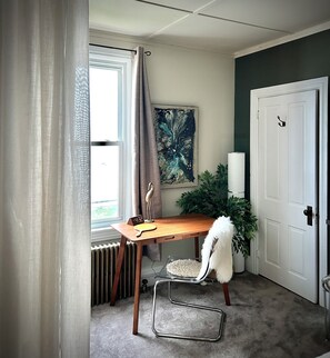 A room with a wooden desk, a chair, a radiator, a door, and a window with curtains.