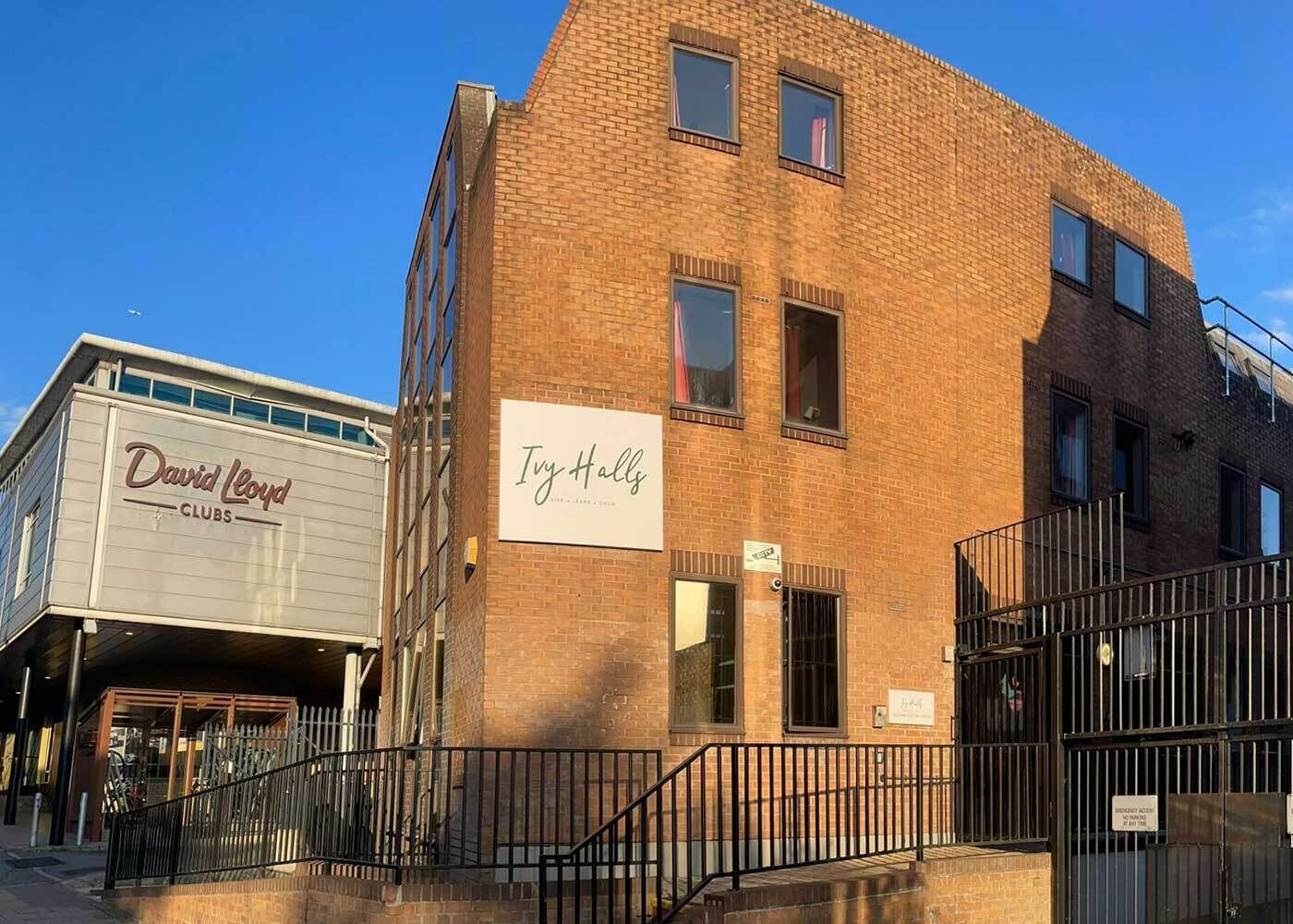 Een gebouw van baksteen met een bordje voor 'Ivy Halls' en een aangrenzend gebouw met de tekst 'David Lloyd CLUBS'.